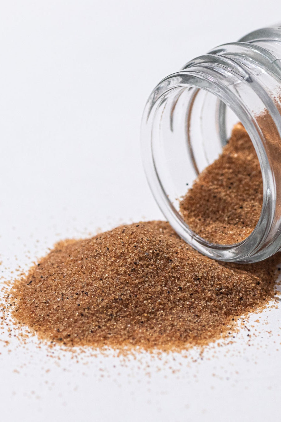 Glass jar of brown sand spilling onto a white surface